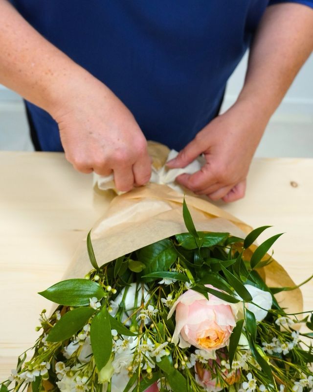 Un mazzo di rose e fiori di cera avvolto a mano nella carta kraft