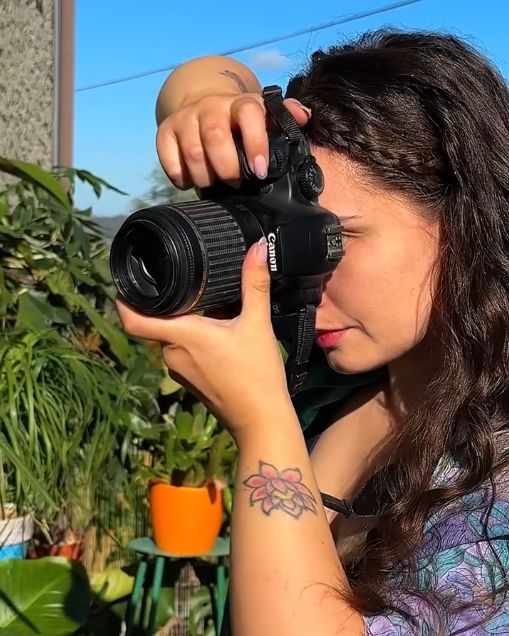 Valentina scatta una foto con la reflex, tra piante in vaso sotto un cielo azzurro